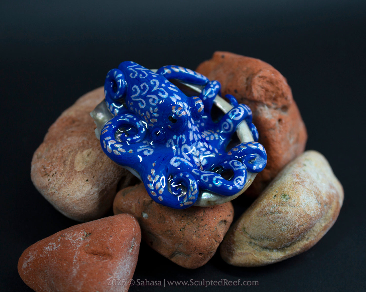Blue and white octopus sculpture on a pile of brown stones with a dark background